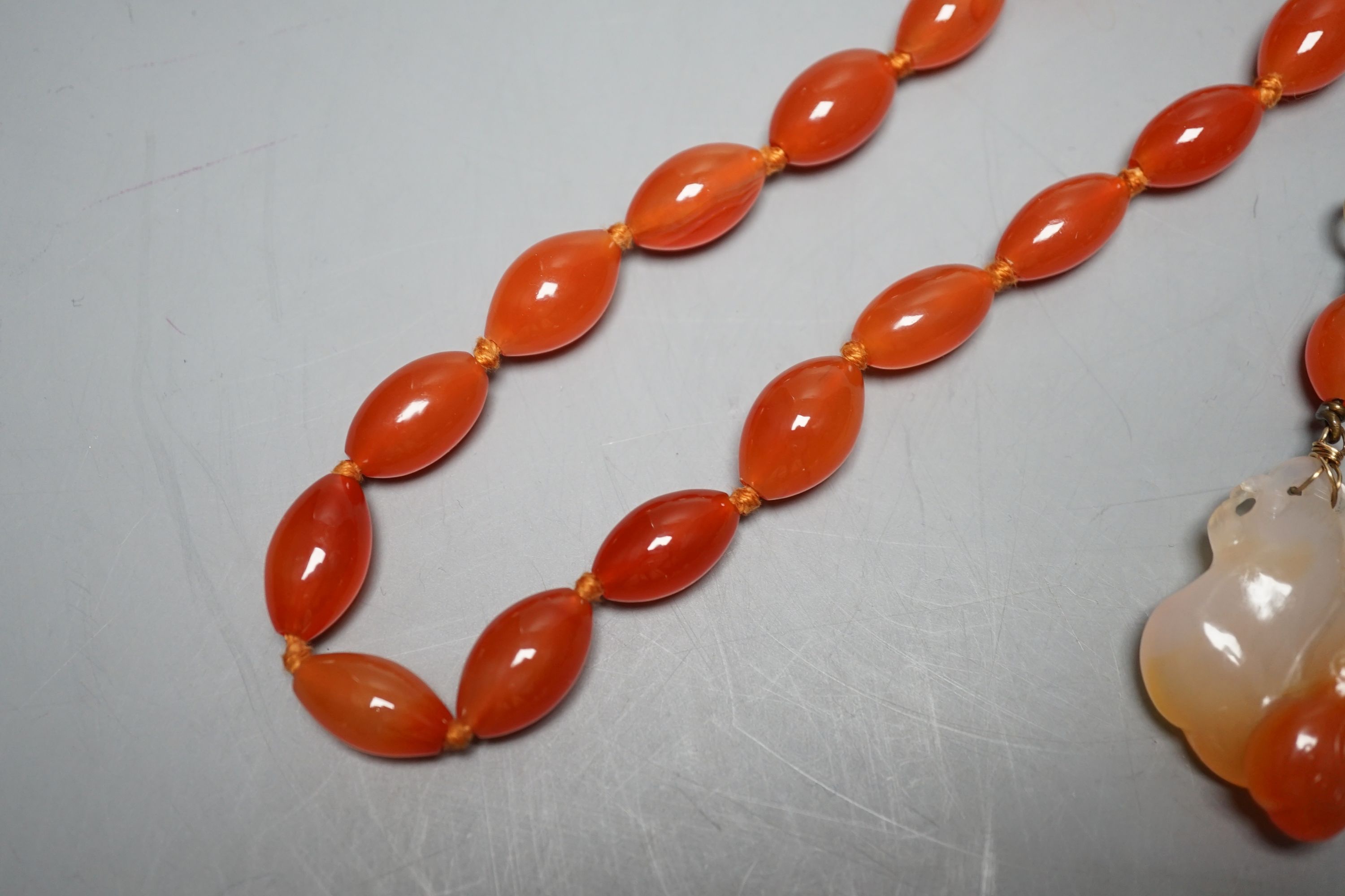 Two carved agate and carnelian bead pendants and a carnelian bead necklace, 48cm.